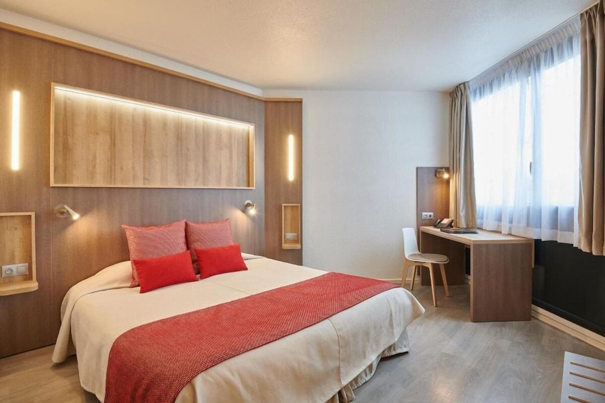 A hotel room with a large bed, a desk, and a chair.