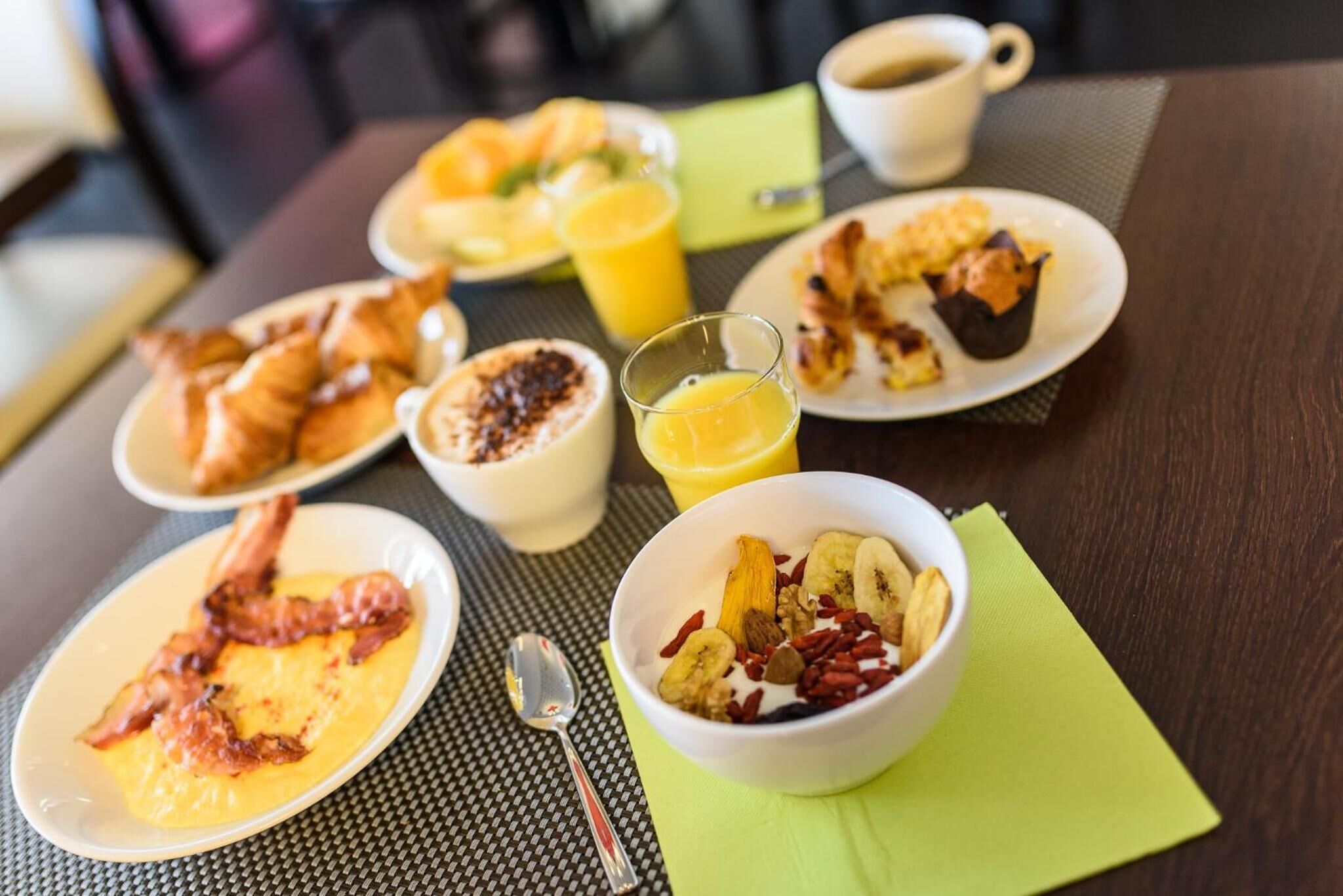 A breakfast setting with plates of food, a bowl of fruit, and a glass of orange juice on a table.