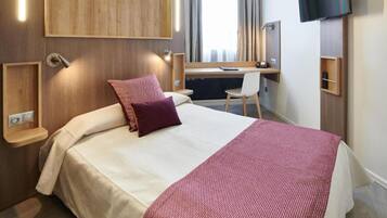Una habitación de hotel con cama, escritorio, silla, televisión y ventana con cortinas.
