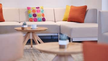 A modern living room with a beige sofa, colorful pillows, and two round wooden tables with cups and small plants.