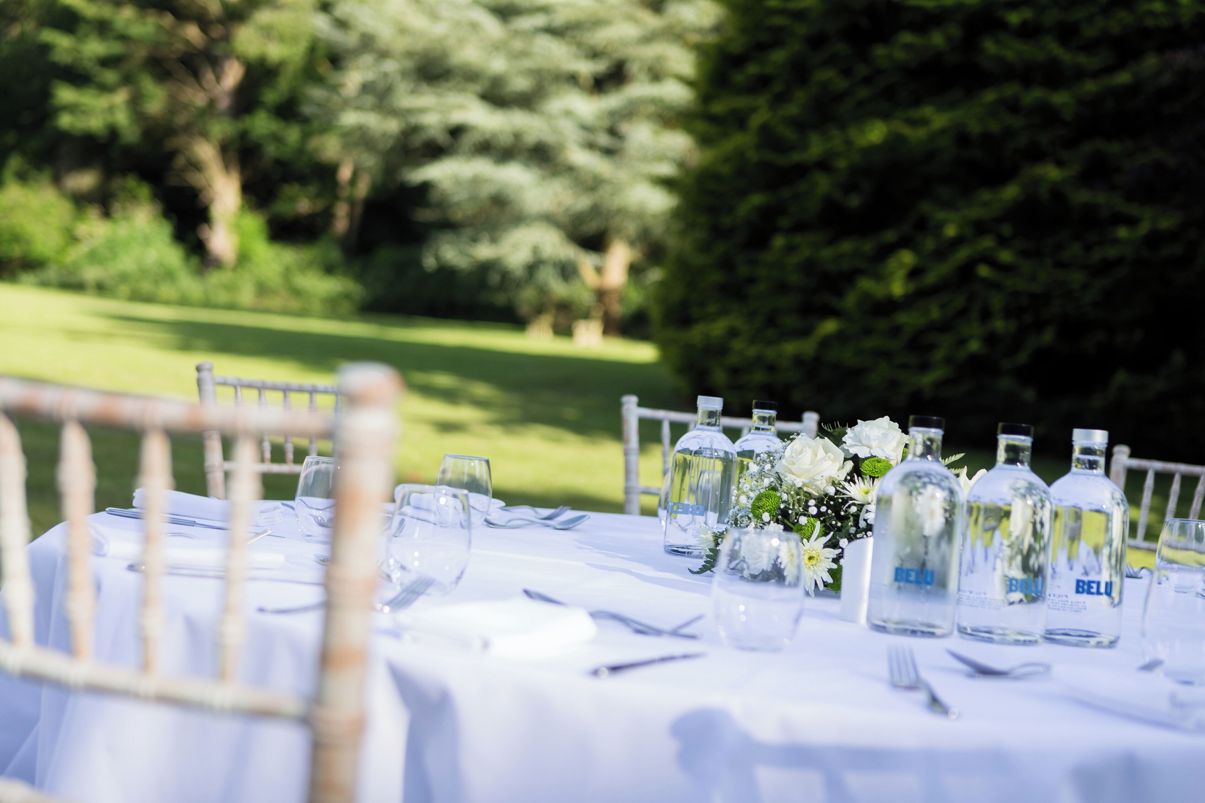 A table set outdoors with clear glass bottles, white tablecloth, and a floral centerpiece.