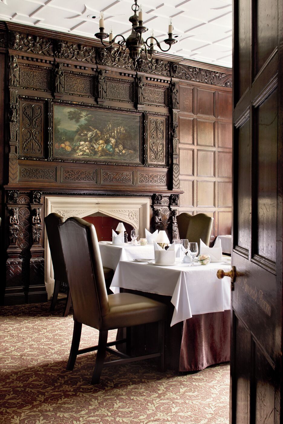 A dining room with a fireplace, ornate wood paneling, and a chandelier.