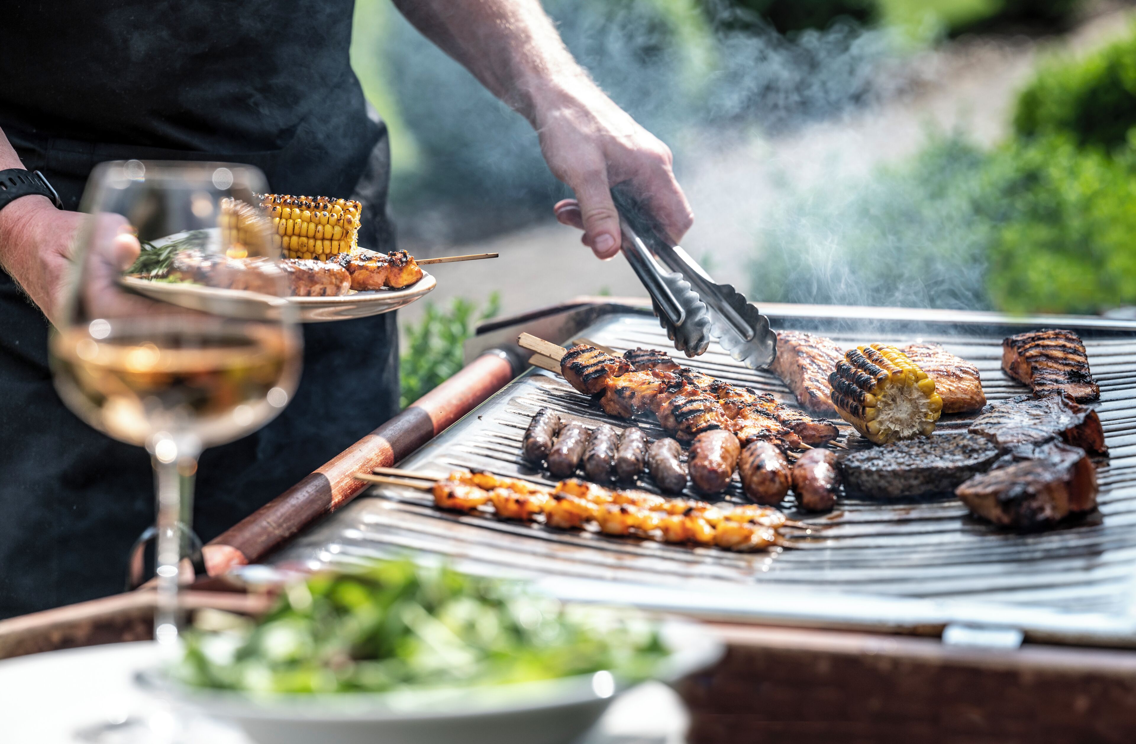 A person grilling various meats and vegetables on an outdoor grill.