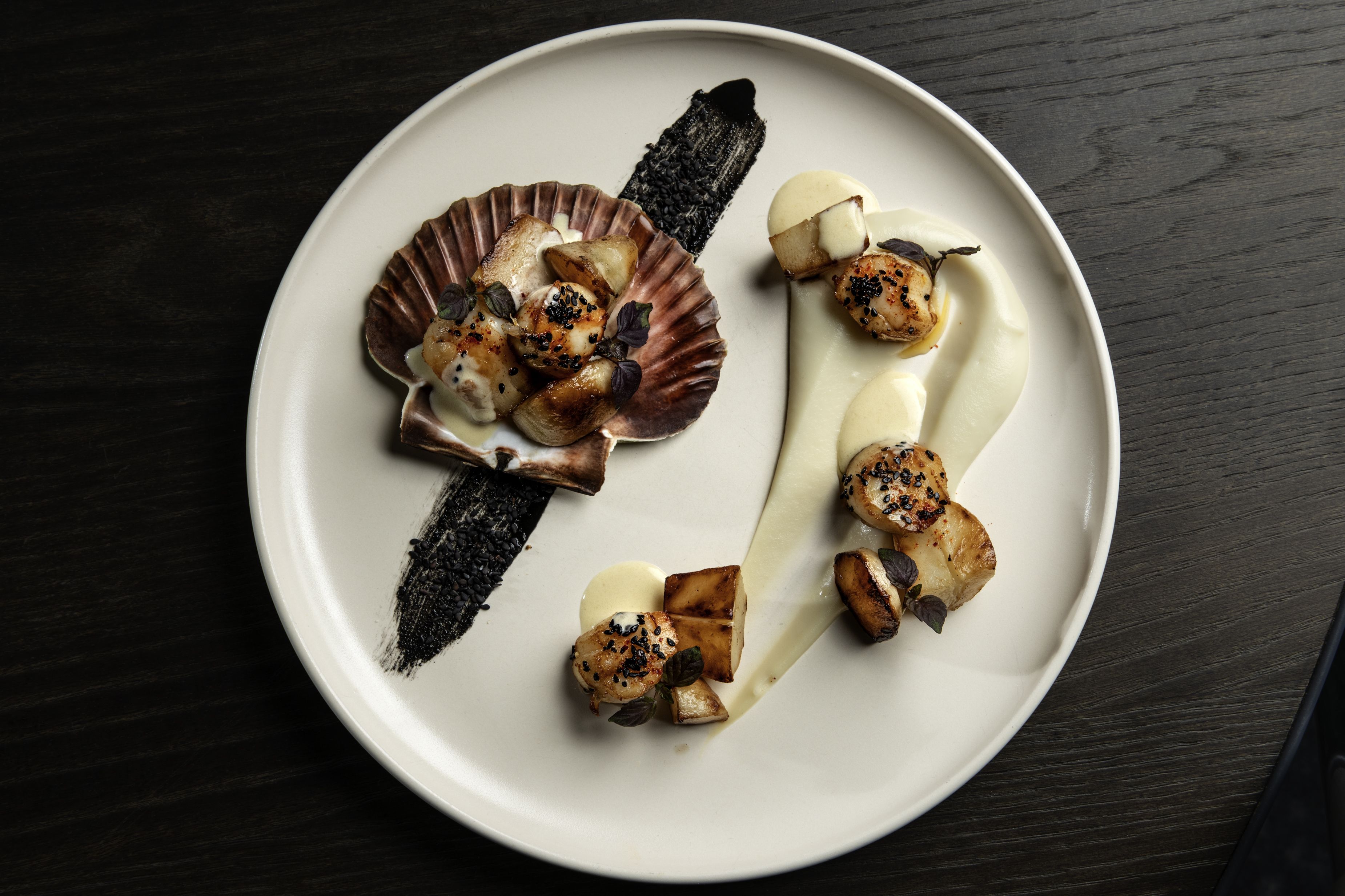 A plate of food with various items including scallops, potatoes, and a piece of black squid ink.