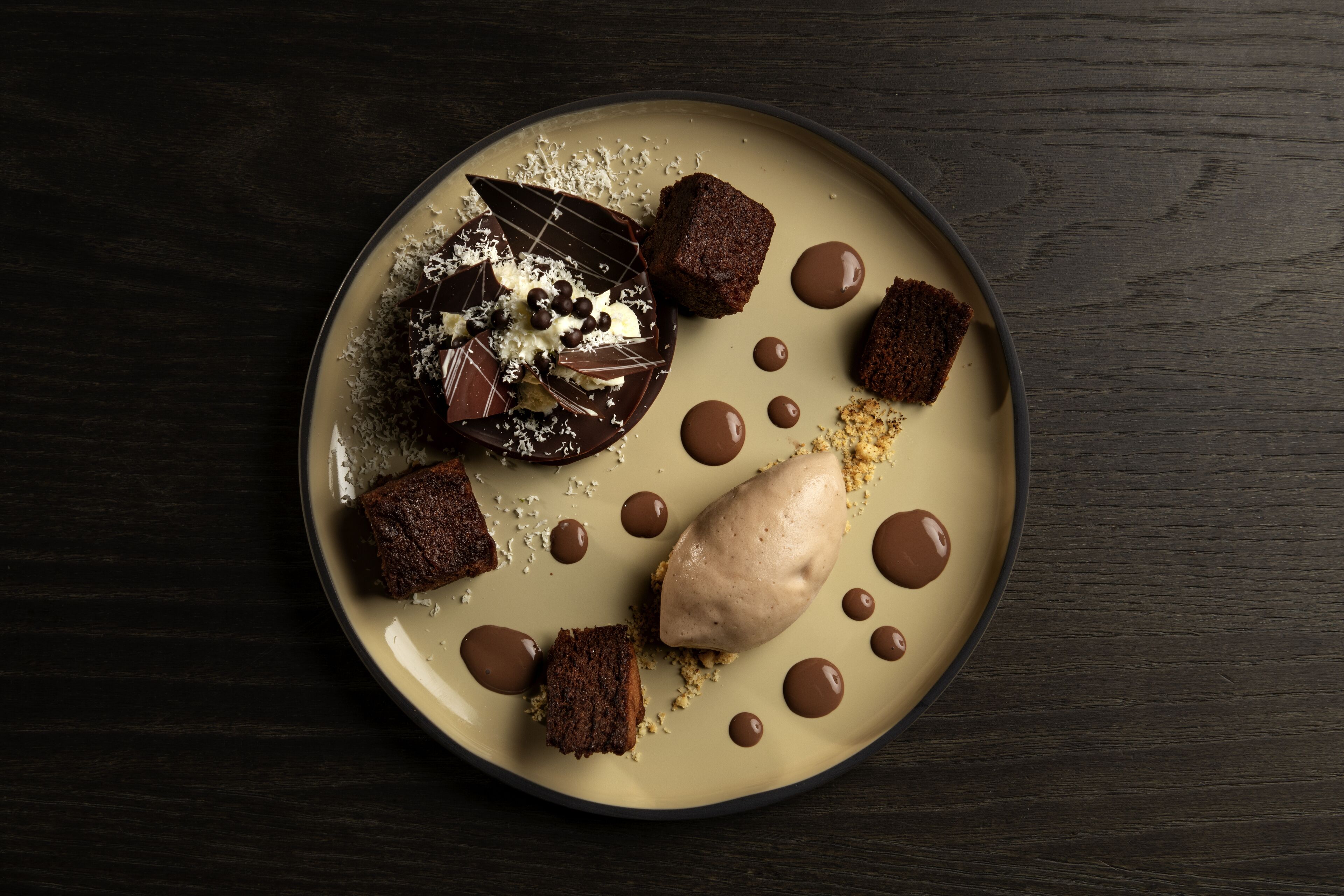 Une assiette à dessert contenant divers produits au chocolat et une boule de glace, le tout présenté sur une assiette de couleur beige.