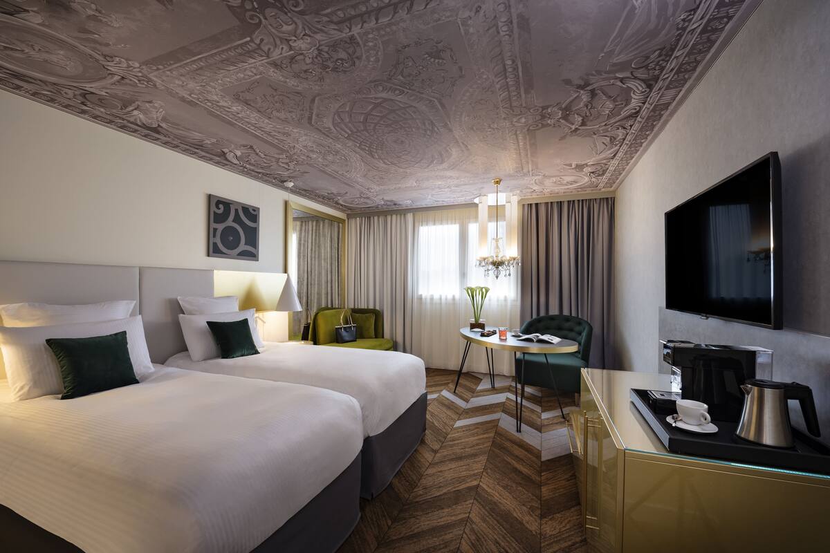 Une chambre d’hôtel avec deux lits, un bureau avec une machine à café, une télévision et un lustre.