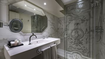 A bathroom with a marble sink, a large mirror, and a shower with ornate wall designs.