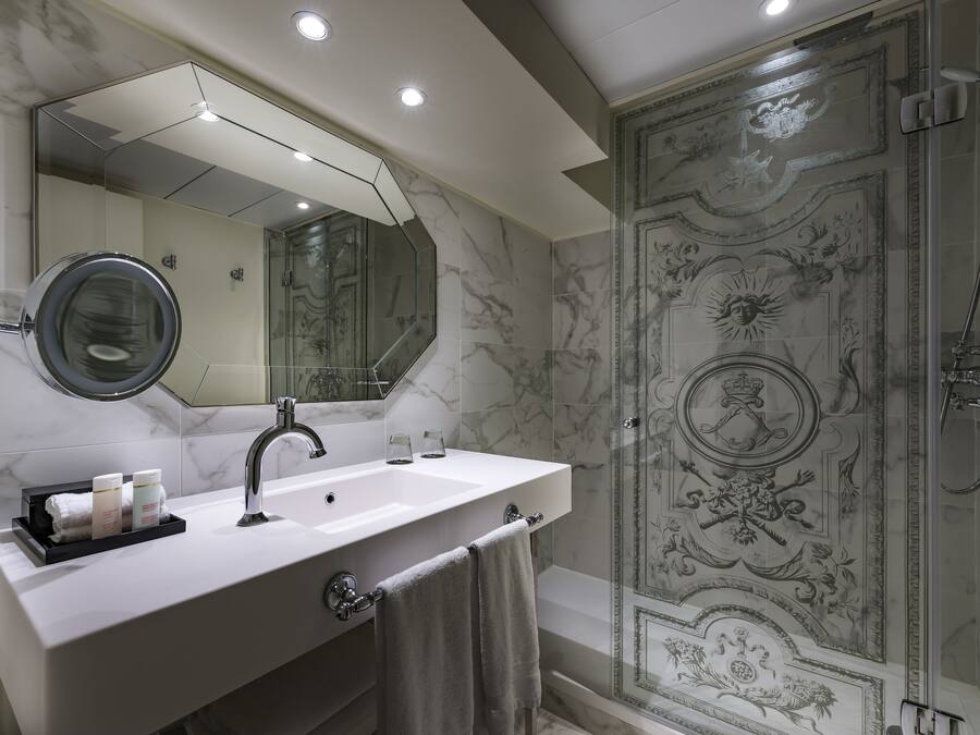 A bathroom with a marble sink, a large mirror, and a shower with ornate wall designs.