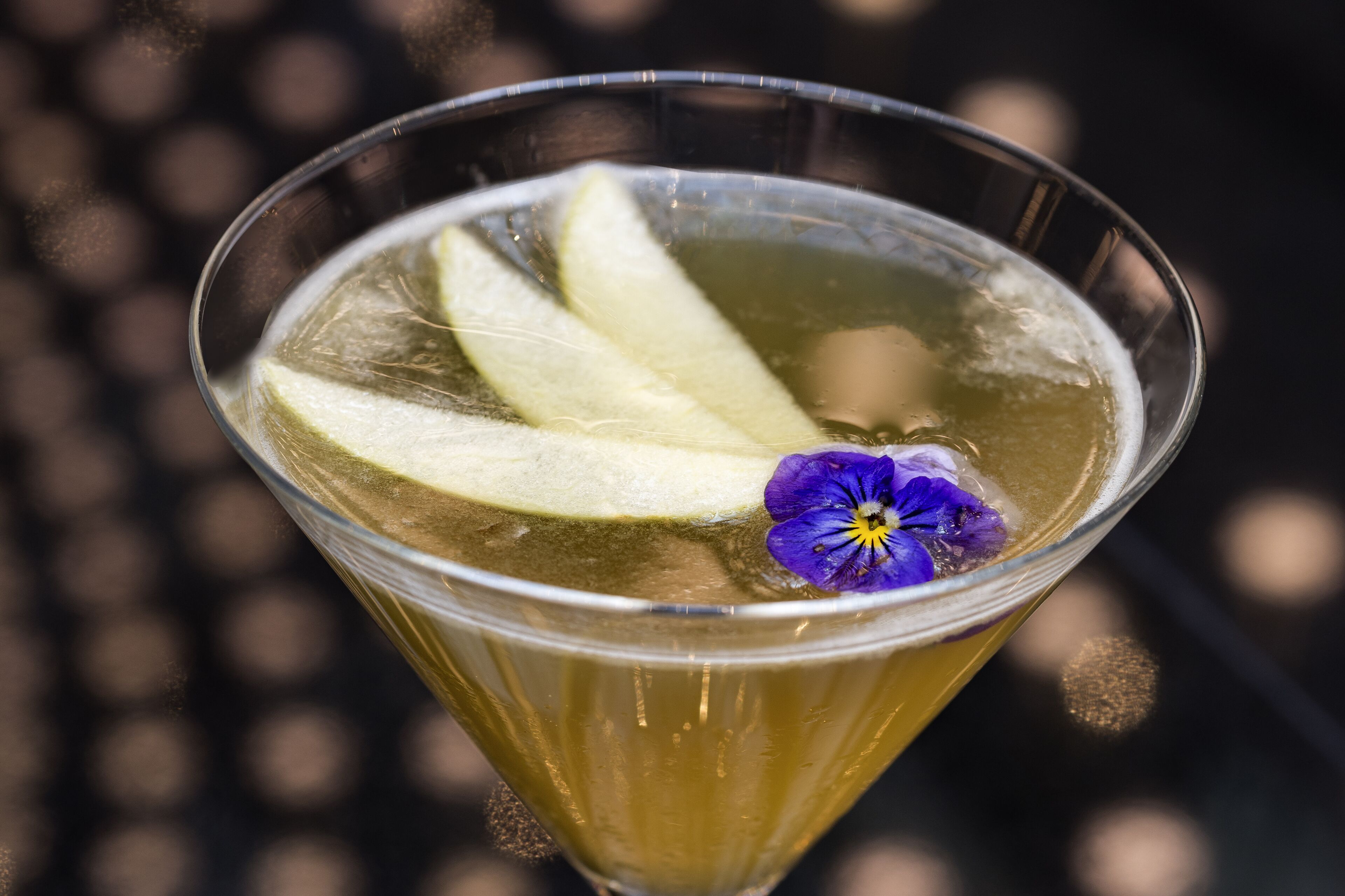 Un verre à martini contenant un liquide transparent, des glaçons et une fleur violette en guise de décoration.