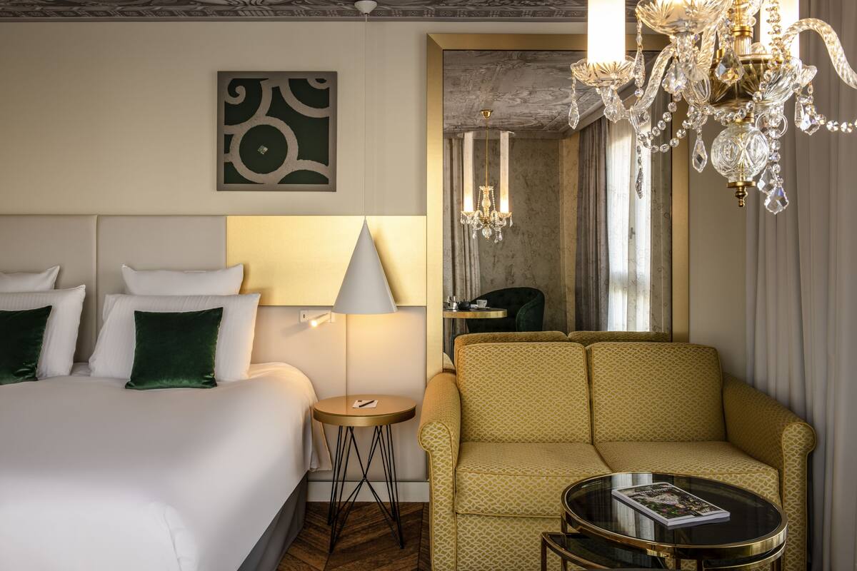 Une chambre d’hôtel avec un lit, un canapé, une petite table, une lampe et un lustre.