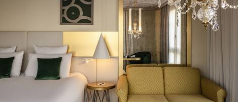 A hotel room with a bed, a sofa, a small table, a lamp, and a chandelier.