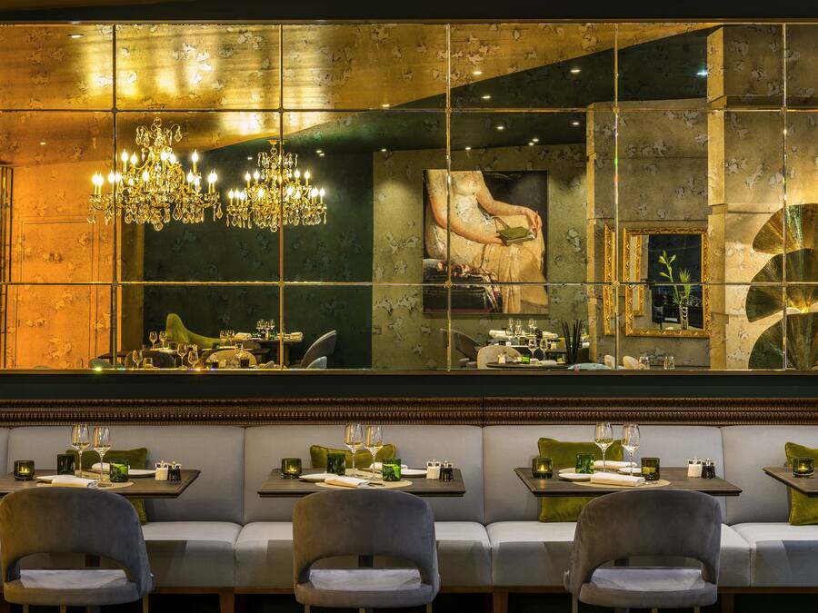 A restaurant with a mirrored wall, a chandelier, and green cushioned seating.