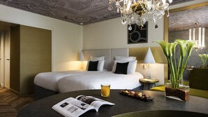 Une chambre d’hôtel avec un grand lit, des lampes de chevet, un coin lecture avec un magazine, un verre de jus d’orange et une plante décorative.