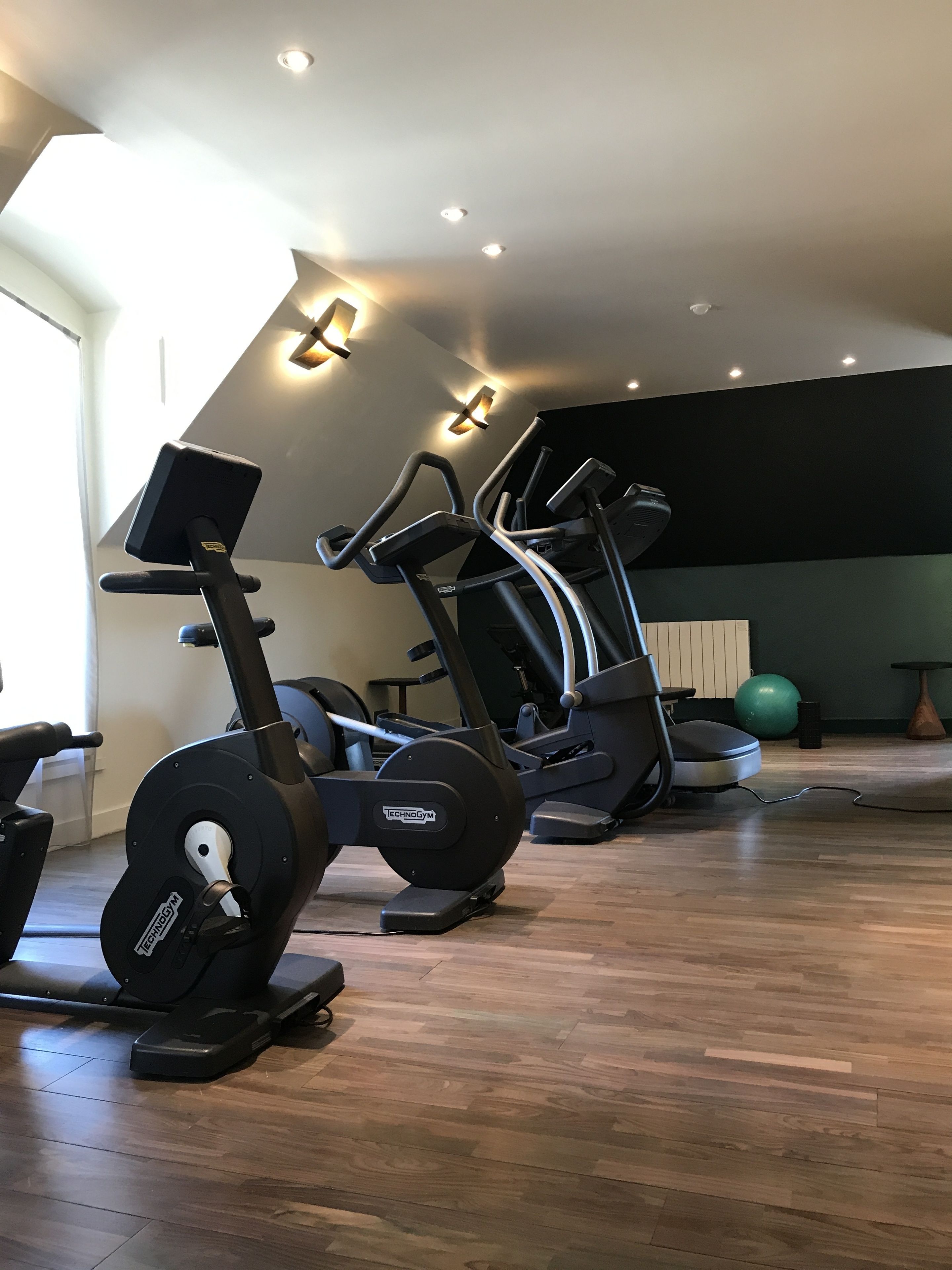 Een sportschool met cardioapparaten, een groene fitnessbal en een houten vloer.