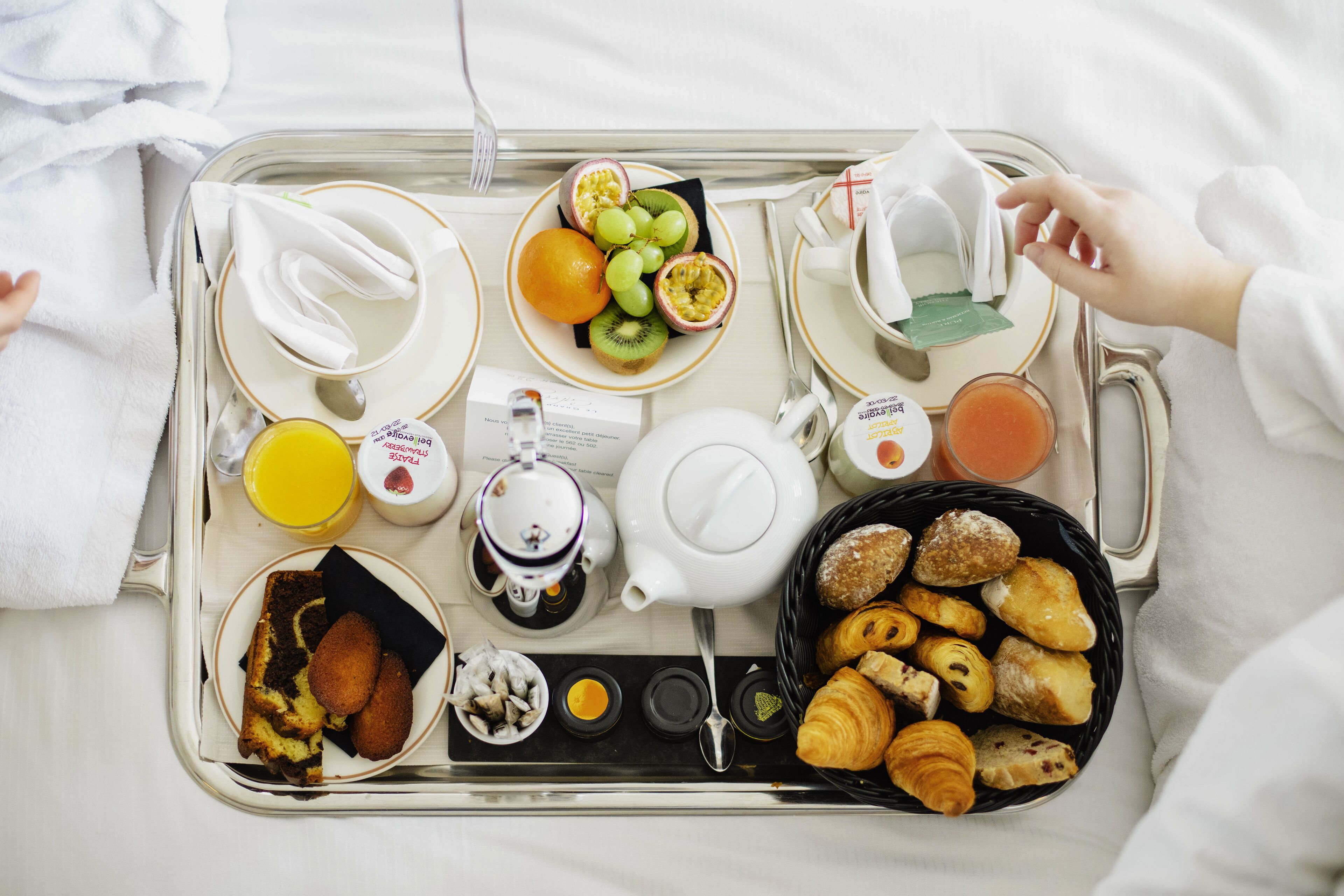 A breakfast tray with croissants, pastries, fruit, juice, and tea on a bed.
