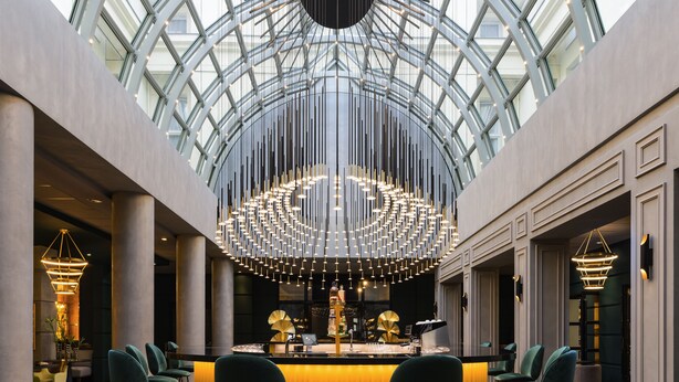 Un hall d’entrée spacieux, doté d’un plafond haut et d’une verrière, avec un bar central agrémenté de tabourets et d’un lustre.