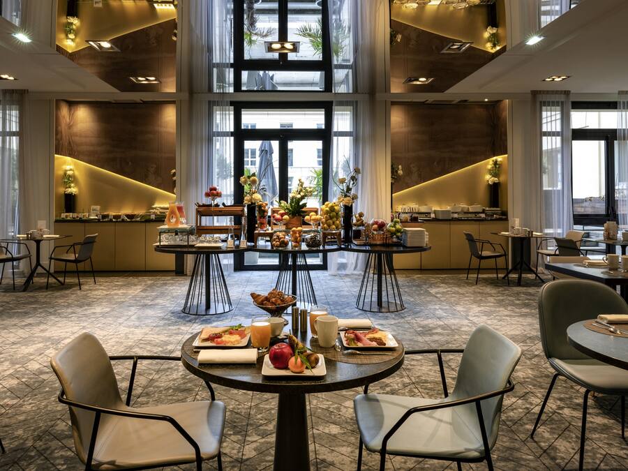 A spacious dining area with multiple tables and chairs, featuring a central table with a variety of dishes and a decorative centerpiece.