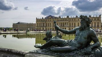 A statue of a seated figure with a child by a reflective water body, in front of a large historic building.