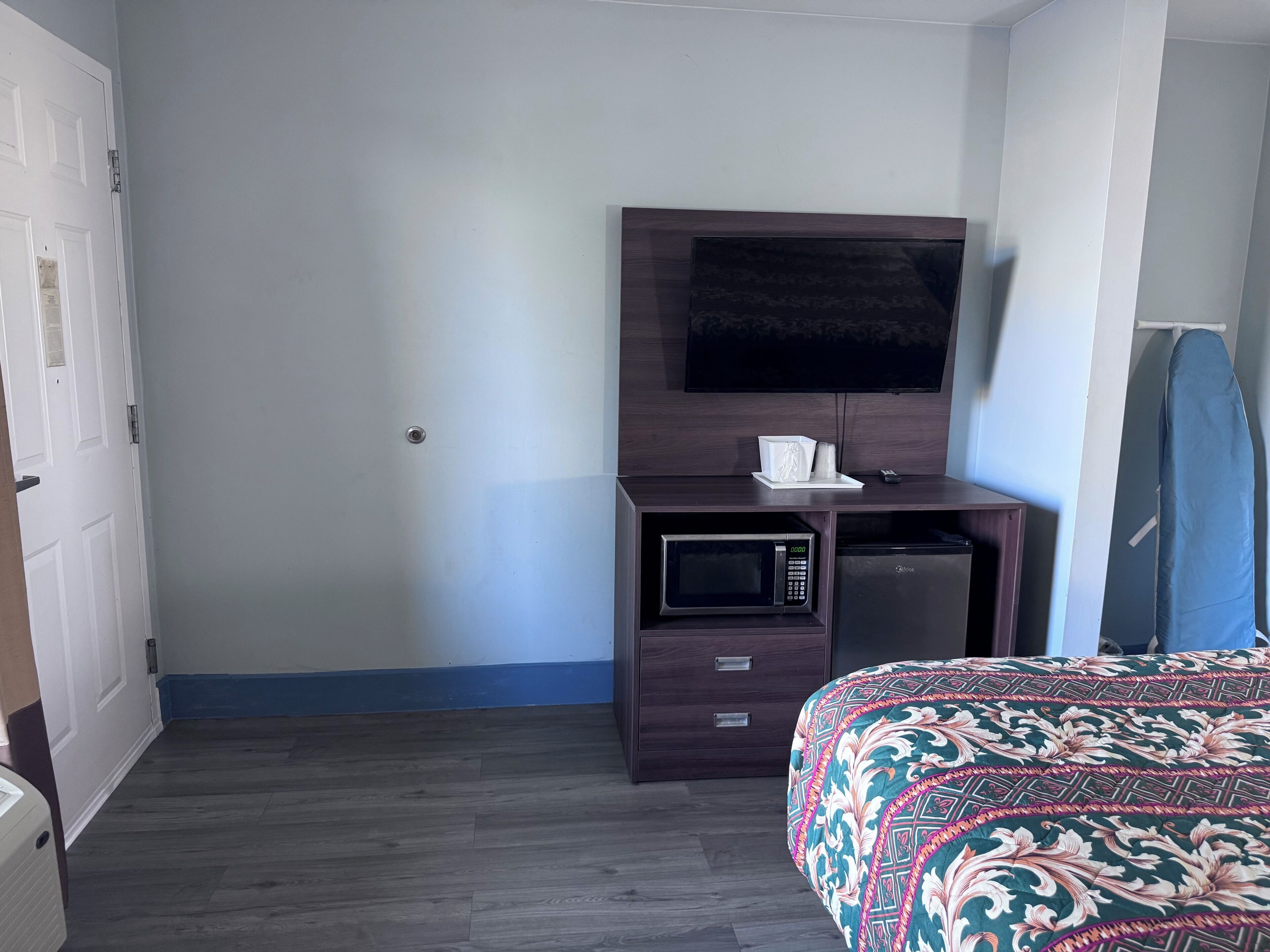 Une chambre d’hôtel comprenant un lit, un bureau avec un micro-ondes, une télévision et un petit placard.