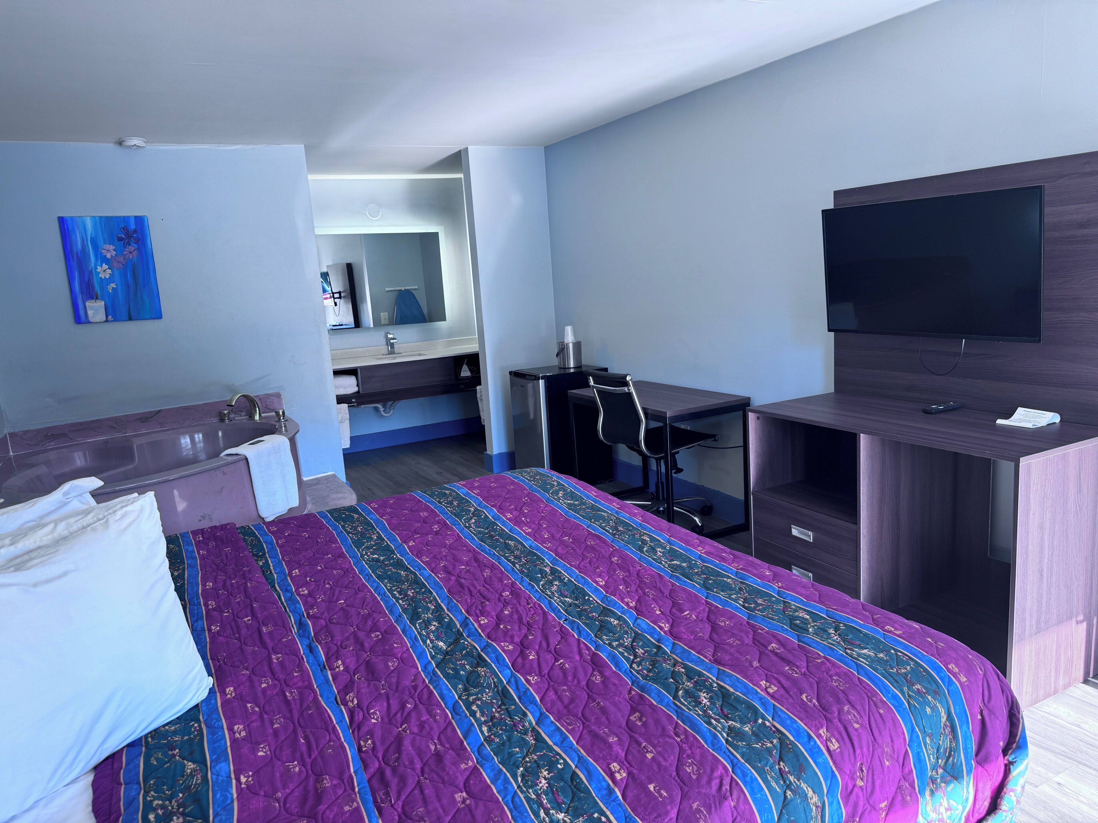 Una habitació d'hotel amb un llit, una taula de treball, un televisor i un bany.