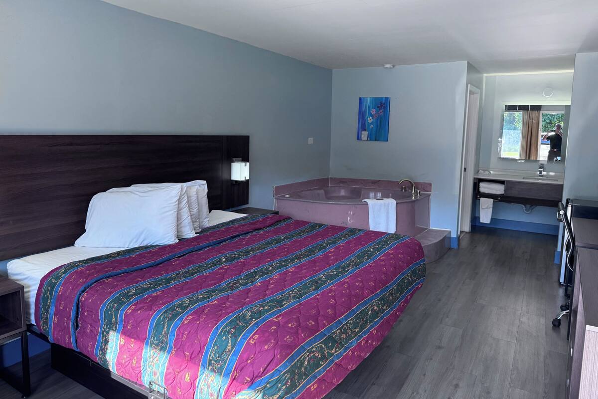 A hotel room with a large bed, a separate bathroom with a bathtub, a vanity with a mirror, and a small desk.