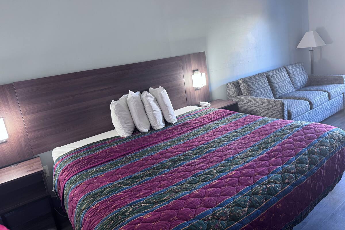 A hotel room with a large bed, a nightstand, a sofa, and a lamp.