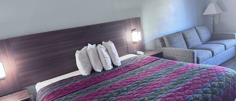 Una habitación de hotel con una cama grande, una mesita de noche, un sofá y una lámpara.