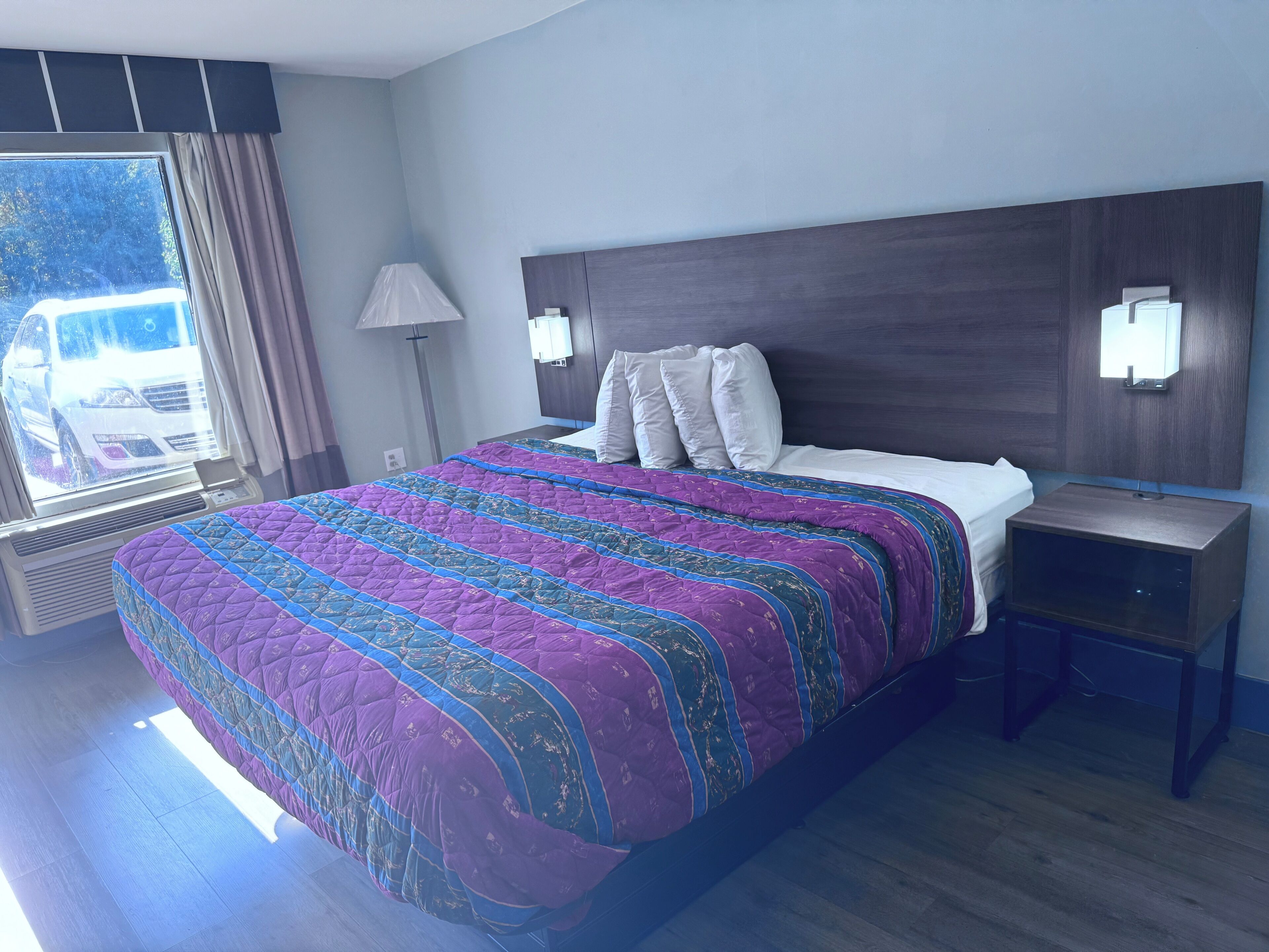 Una habitación de hotel con una cama grande, una mesita de noche, una lámpara y una ventana con cortinas.