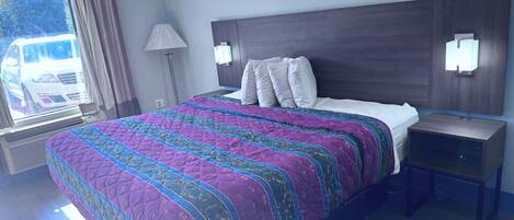 Una habitación de hotel con una cama grande, una mesita de noche, una lámpara y una ventana con cortinas.