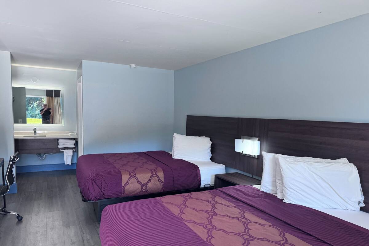 A hotel room with two beds, a bathroom with a mirror, and a small desk.
