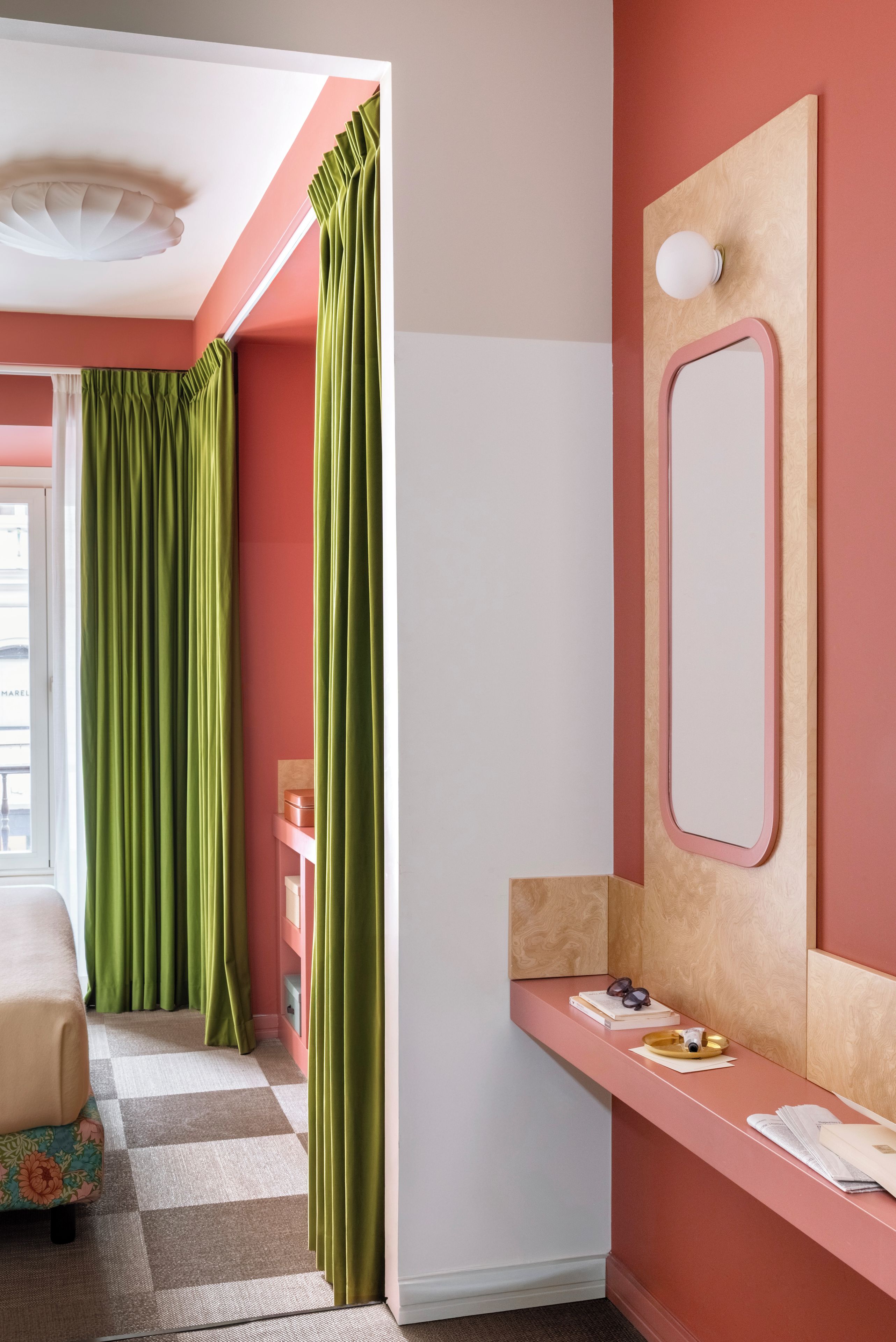 A room with a checkered floor, a bed, a vanity with a mirror, and green curtains.