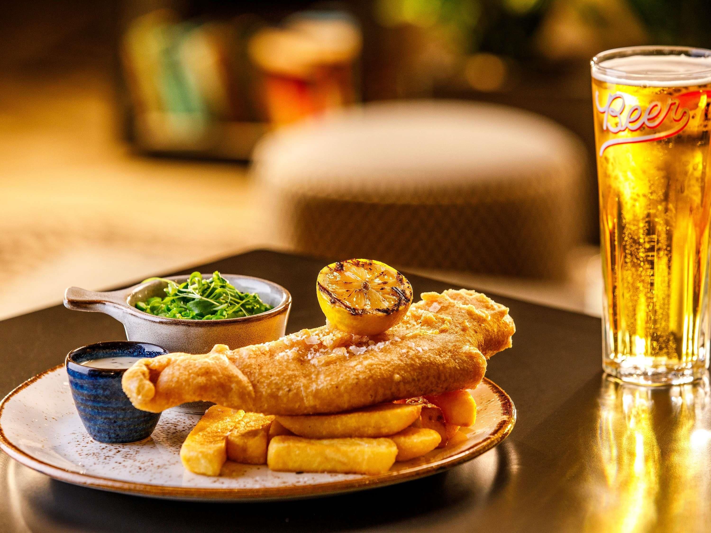 A plate of fish and chips with a side of greens and a glass of beer.