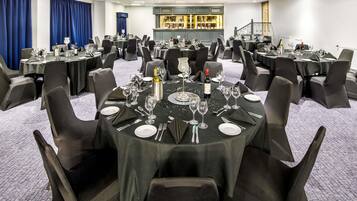 Un salón de conferencias con mesas redondas, sillas negras y una zona de bar.