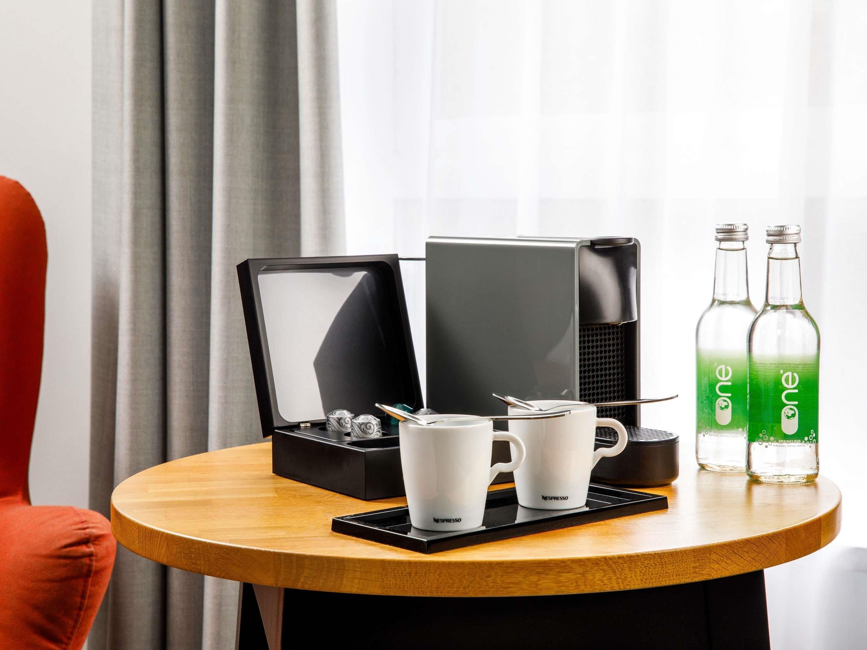 A coffee machine, two Nespresso cups, and two One brand bottles on a wooden table.