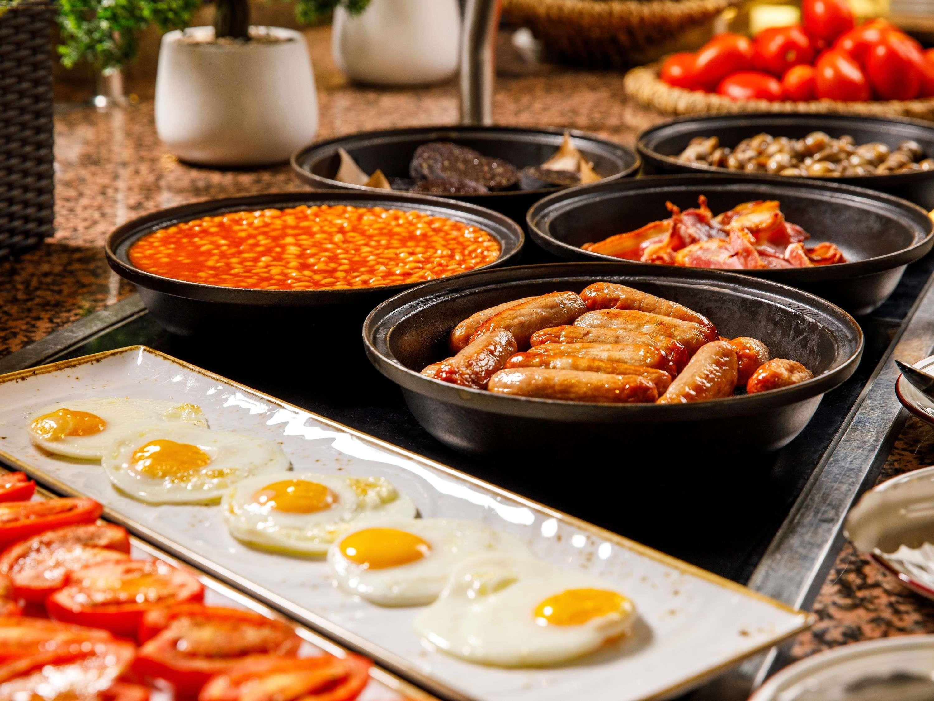 A breakfast buffet with various dishes including eggs, sausages, beans, and tomatoes.