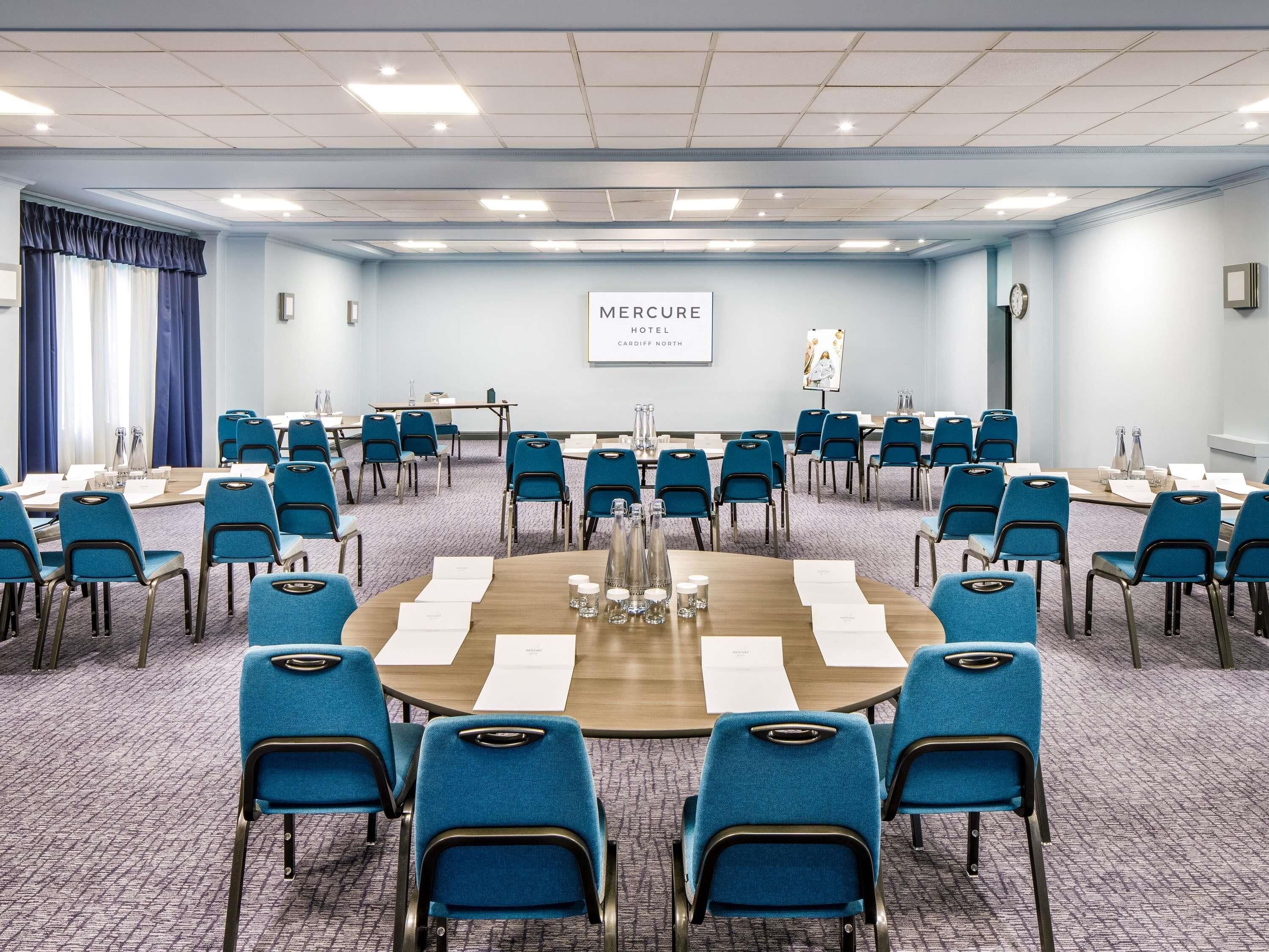 Kokoushuone, jossa on pyöreä pöytä, siniset tuolit ja kyltti, jossa lukee Mercure Hotel Cardiff North.