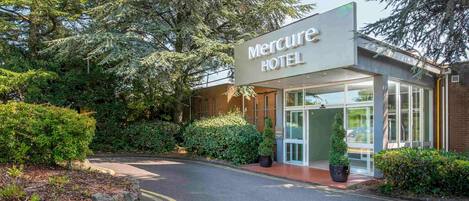 Entrada de un hotel con un cartel que dice 'Mercure HOTEL', rodeada de follaje y un camino curvo.