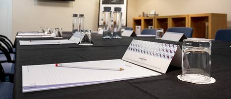A conference room with a black table, lined notepads, a pencil, a glass of water, and a name card.