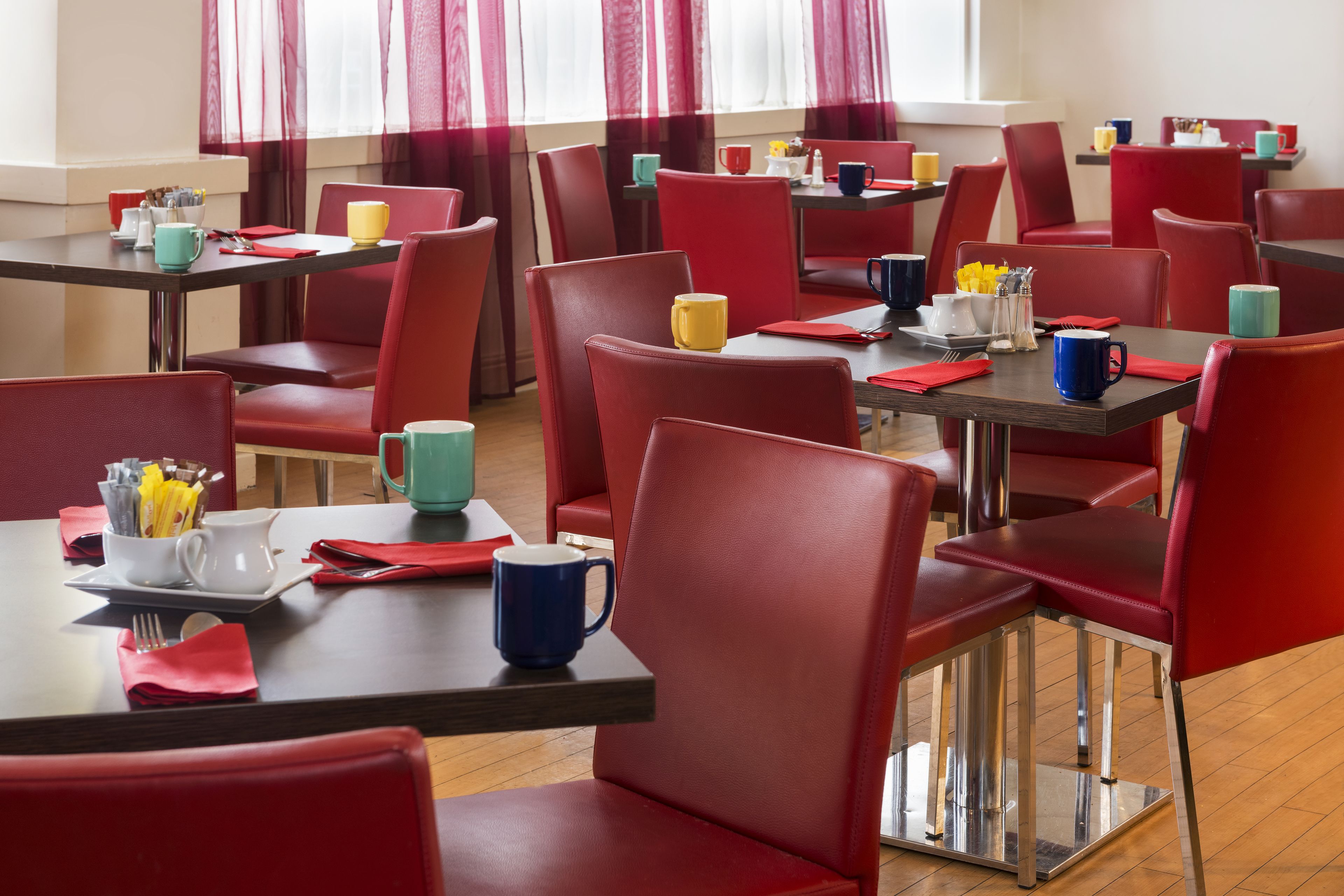 Un comedor con sillas y mesas rojas, cada juego con una taza, platillo y cubiertos.