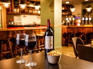 A bar setting with two wine glasses, a bottle of wine, and a bowl of nuts on a table.