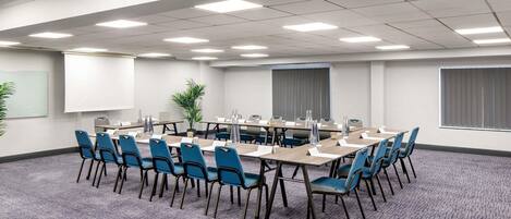 A conference room with a round table, blue chairs, a projector screen, and a potted plant.