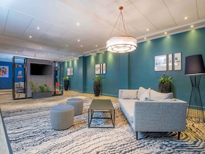 A modern lounge area with a sofa, ottomans, a coffee table, and a TV screen.