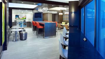 Een moderne hotellobby met een bar, zitgedeelte en een televisiescherm.