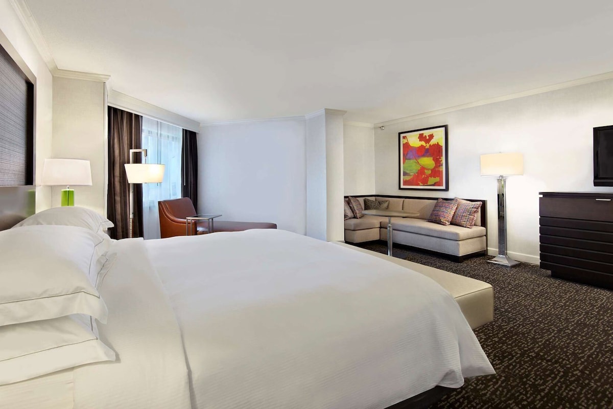 Une chambre d’hôtel avec un grand lit, un canapé, un bureau, une chaise, un téléviseur à écran plat et un tableau au mur.