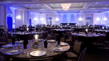 A large banquet hall with round tables set for dining, featuring candle centerpieces and formal table settings.