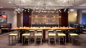 Une salle de conférence avec une longue table, des chaises vertes et un lustre moderne.