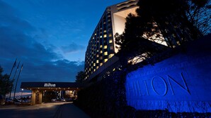 Entrada de um hotel Hilton ao entardecer, com janelas iluminadas e céu limpo.