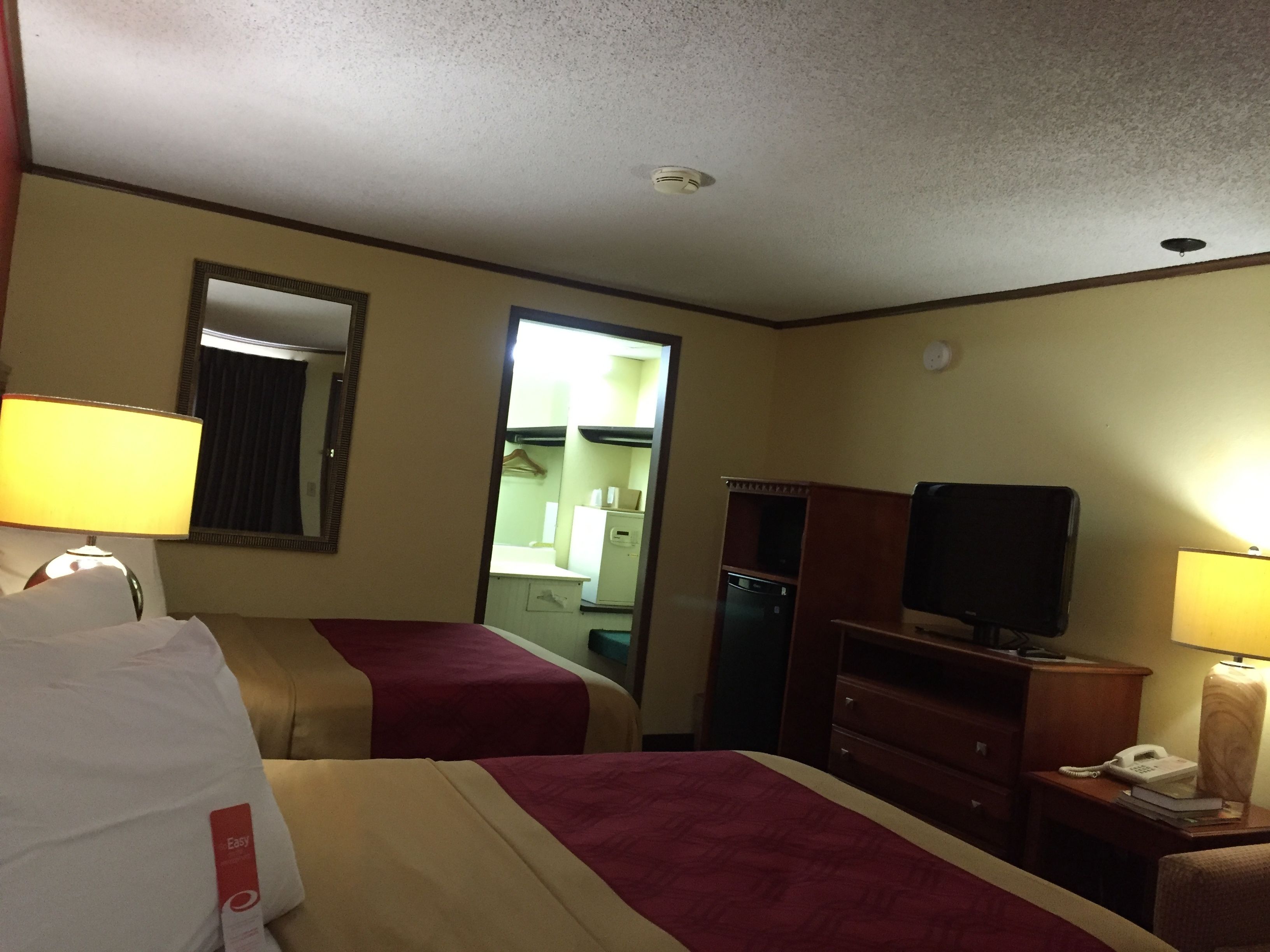 A hotel room with two beds, a television, a desk with a lamp, and a mirror.