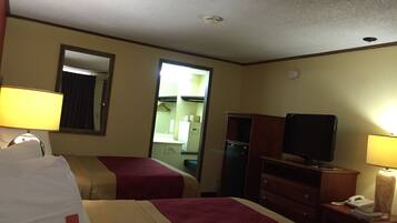 A hotel room with two beds, a television, a desk with a lamp, and a mirror.