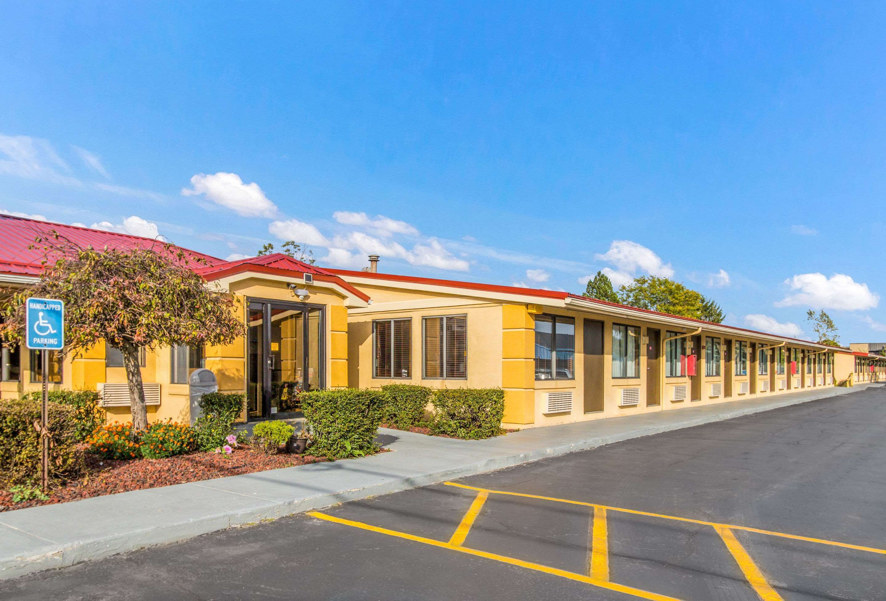 A motel with a red roof, yellow exterior, and handicap parking sign.
